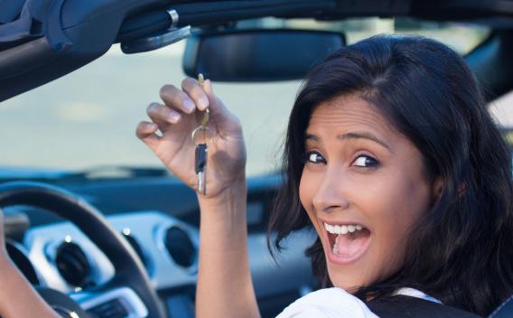 A young, cheerful woman holding up keys to her first new sports car