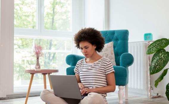 A young woman sitting on a living room floor using a laptop