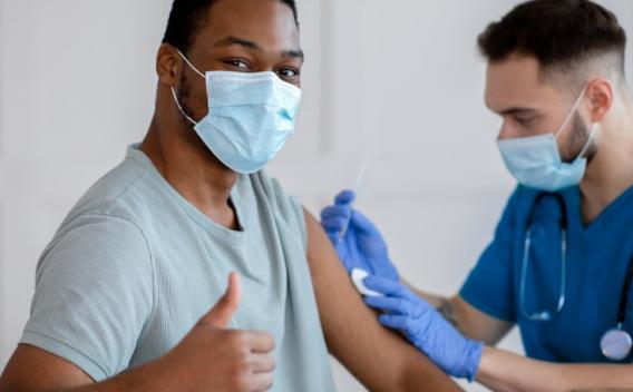 African-American man in mask gesturing thumb up during vaccination