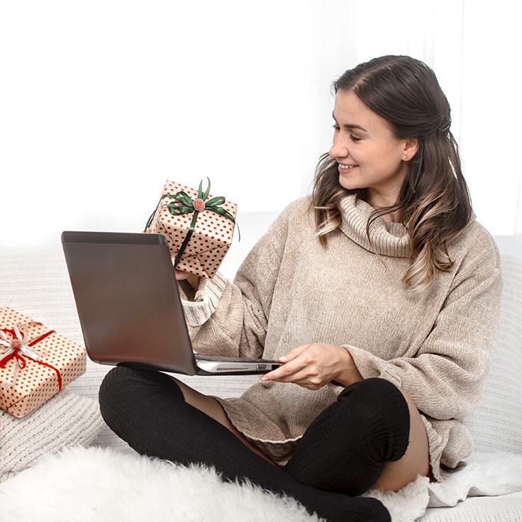 A woman sitting on the floor with a laptop and wrapped presents beside her