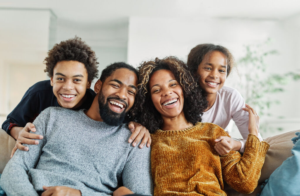 A family of four is sitting on their front porch smiling after opening a checking account at San Francisco Federal Credit Union.