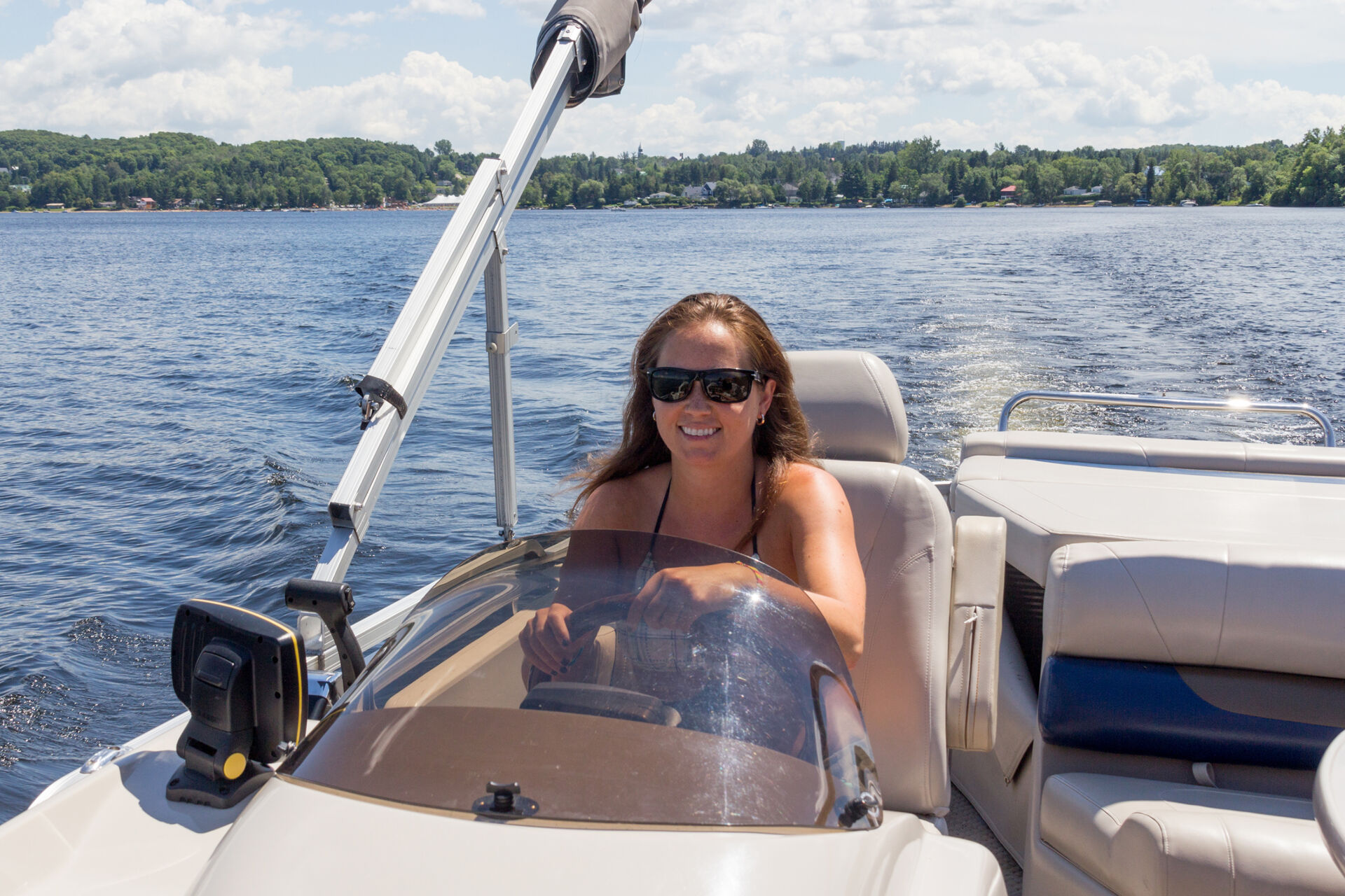 A woman is smiling while she drives the new boat she got with credit union financing.